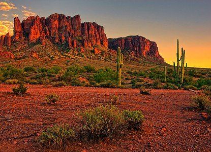 Desert landscape with red rocks, cactus, and a rugged mesa at sunset