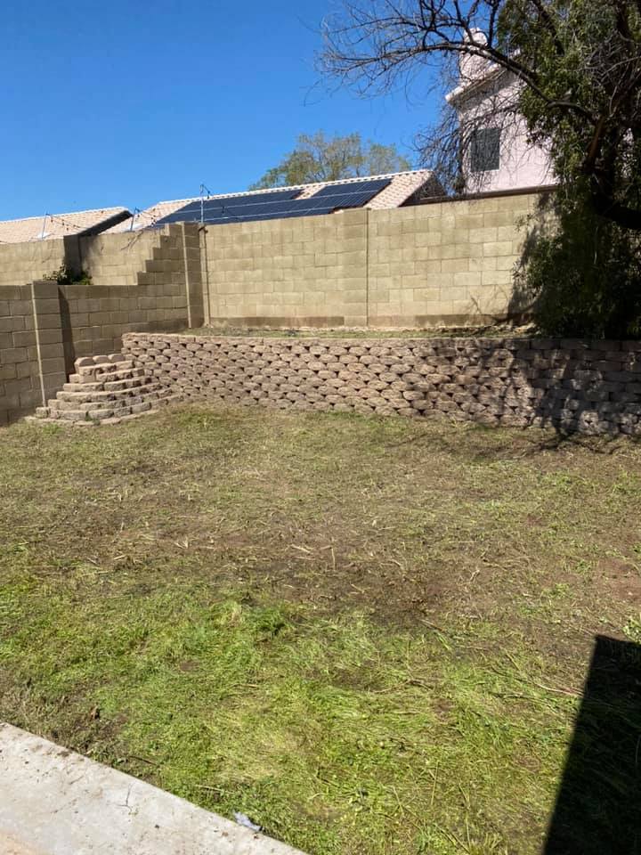 Stone retaining wall around a grassy yard beside a stucco building under a clear blue sky