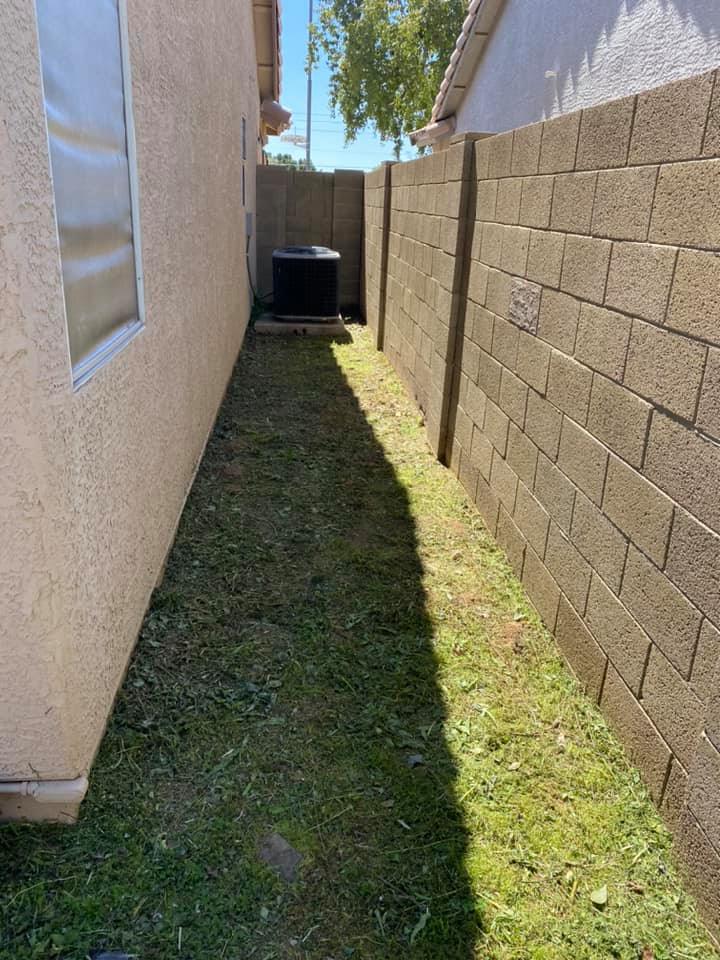 Narrow grassy side yard between a house and cinderblock wall, with an outdoor unit at the end.