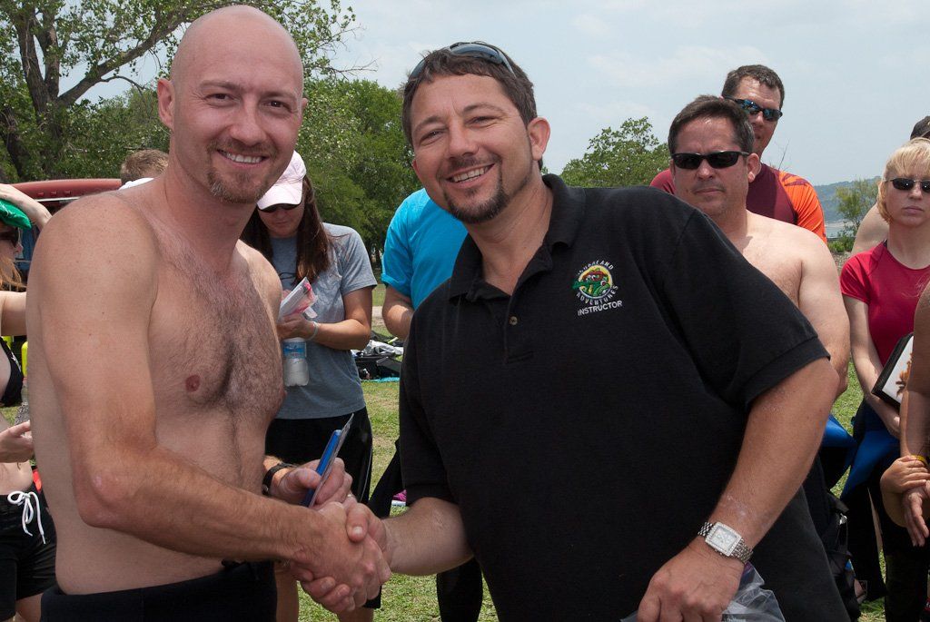 Two men shaking hands outdoors after an event. Other people are in the background.