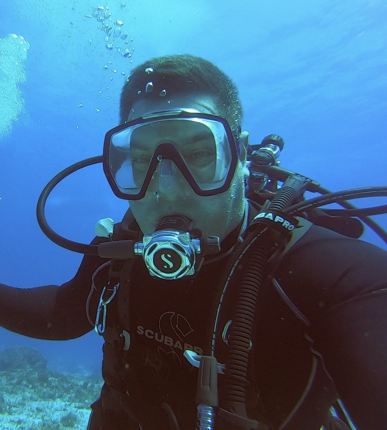 Scuba diver underwater, wearing mask and regulator, with bubbles, looking at camera.