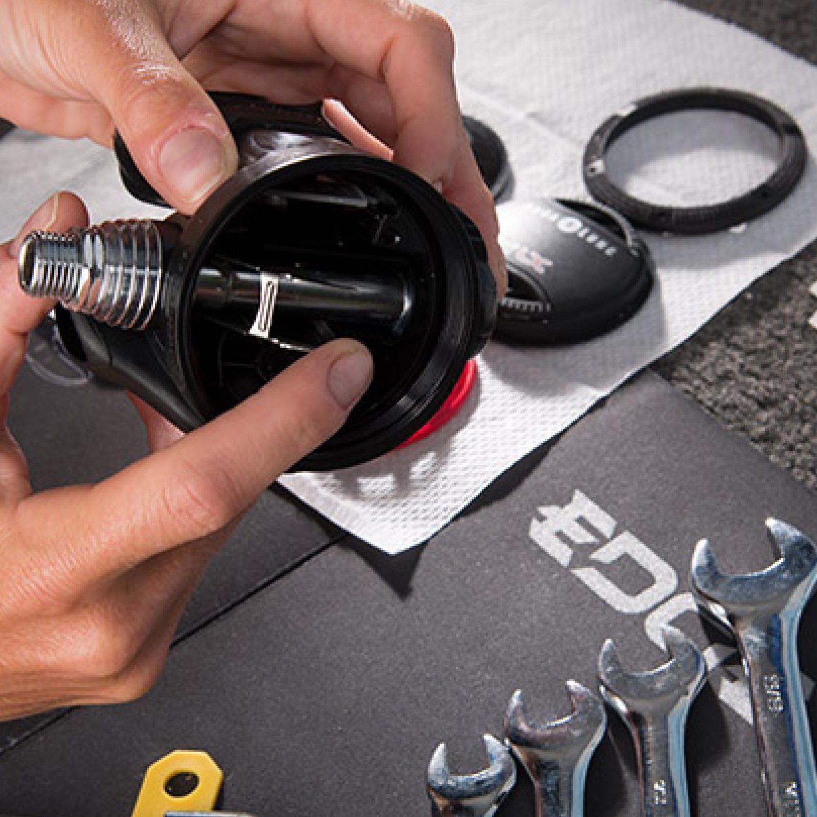 Hands assembling a black scuba regulator, tools on a black surface.