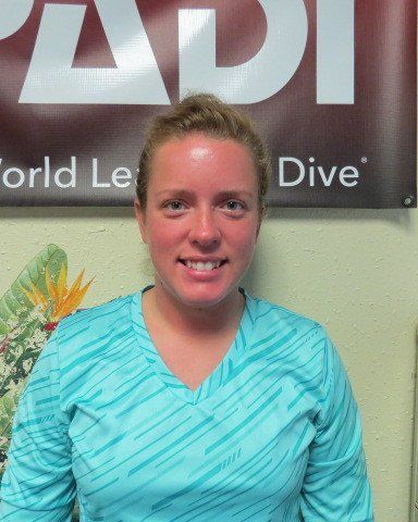 Woman smiling in front of a PADI sign, wearing a blue patterned shirt.