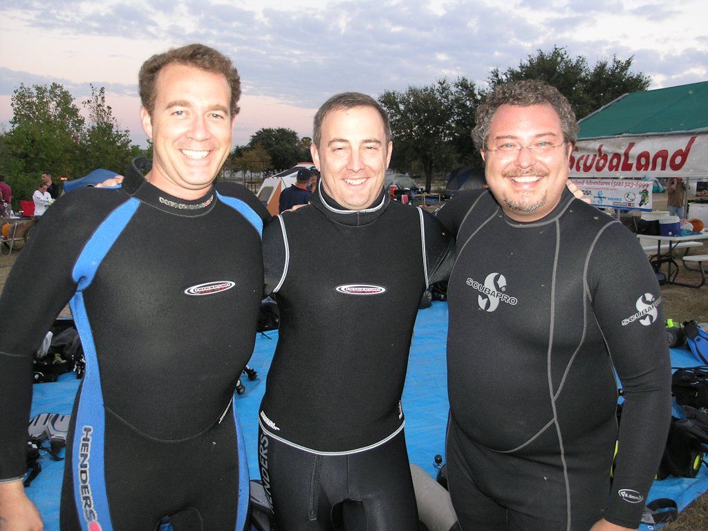 Three people in scuba gear smiling outdoors.