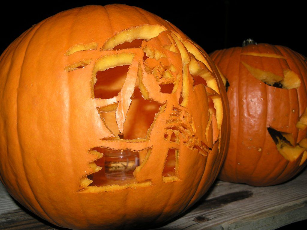 Two carved orange pumpkins, one with a complex design lit from within; dark background.