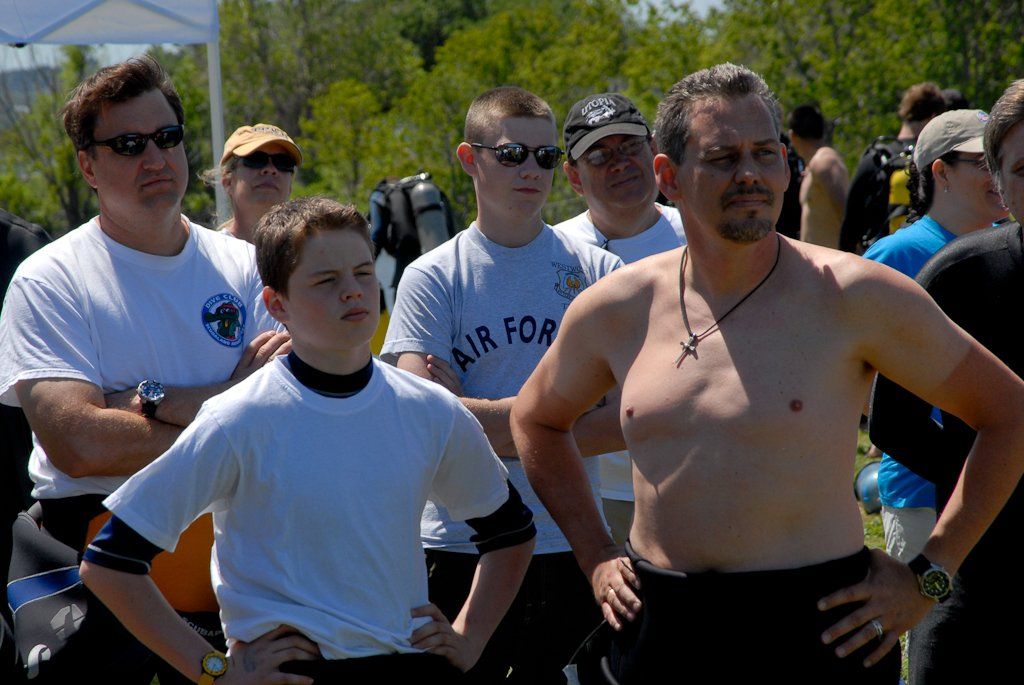 Group of people outdoors; some in swim gear, some wearing sunglasses, observing something.