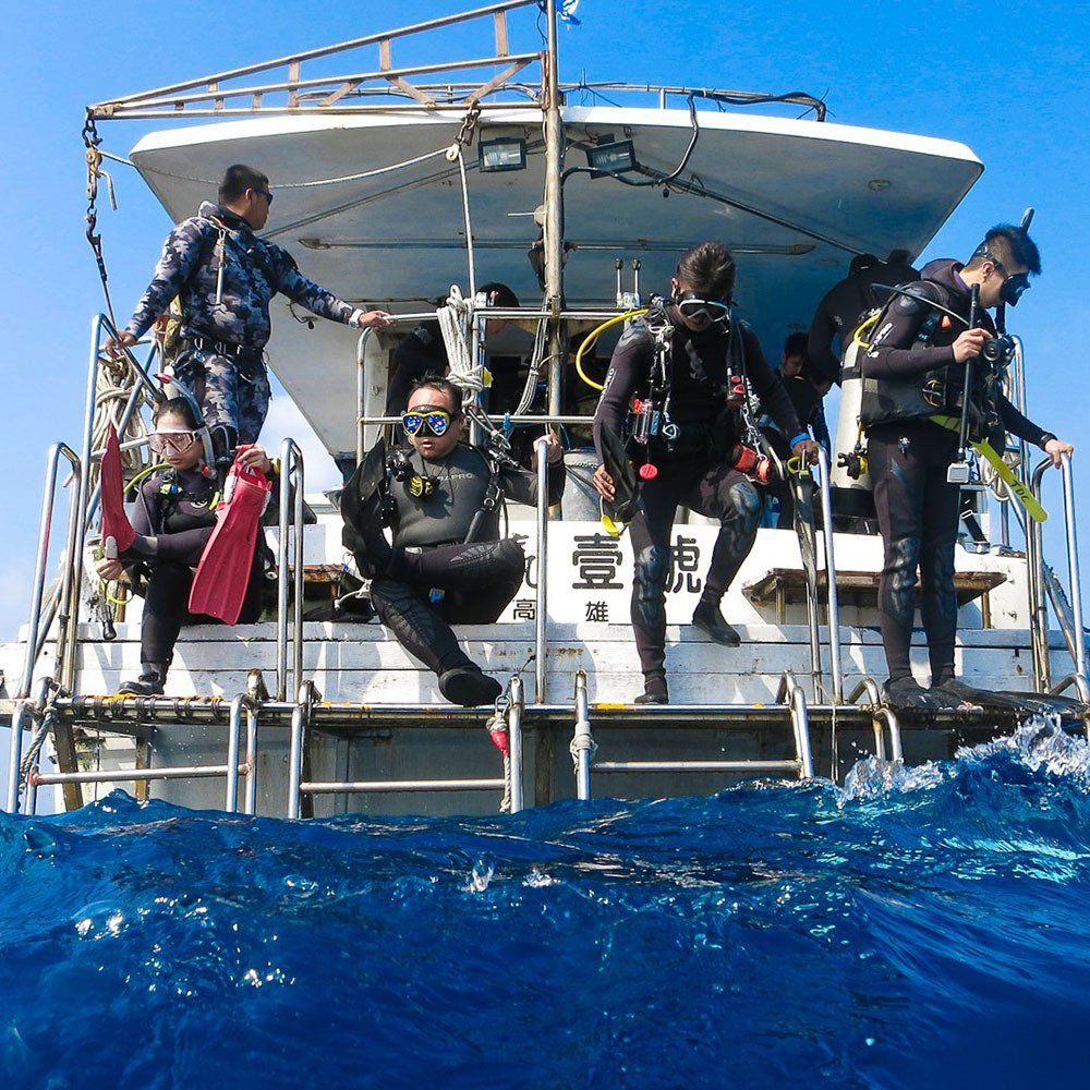 Divers preparing to enter the ocean from a boat. One diver sits, others stand ready, blue water.