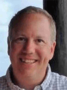 Man smiling, wearing a blue patterned button-down shirt.