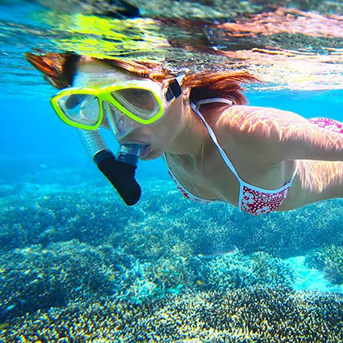 Woman snorkeling, wearing yellow mask and bikini, over coral reef.