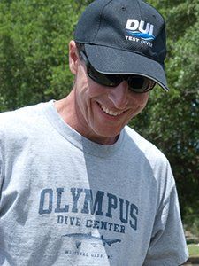 Man wearing sunglasses and a hat smiling, t-shirt reads 