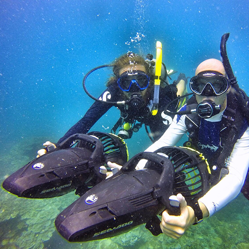 Two scuba divers using underwater scooters in blue water.