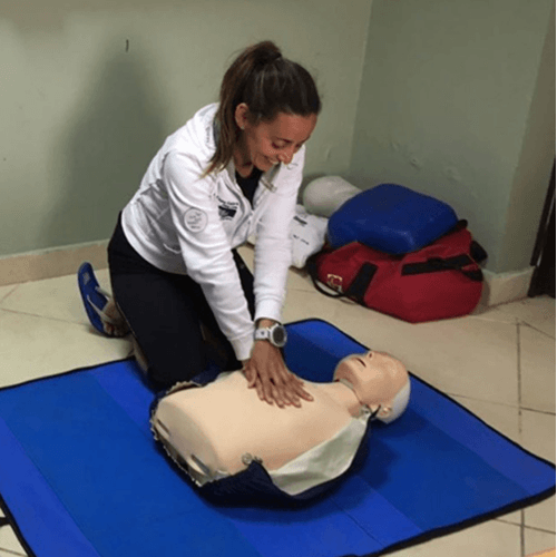 Woman practicing CPR on a training dummy, indoors.