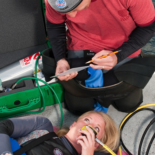Person giving oxygen to diver, filling out a form on a boat.