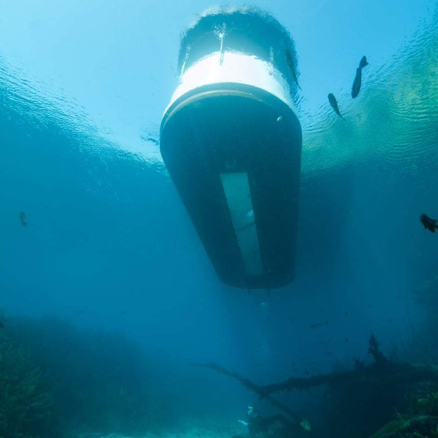 Underwater view of a boat's hull, blue water with visible sunlight and a few fish.