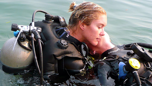 Woman in dive gear leaning on another person in water.