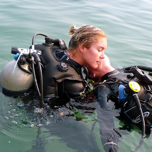 Two divers embrace in water. Blonde woman and man in scuba gear.