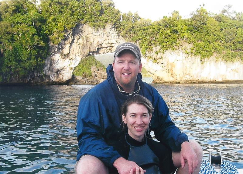 Couple on a boat in front of a natural rock archway in a body of water.