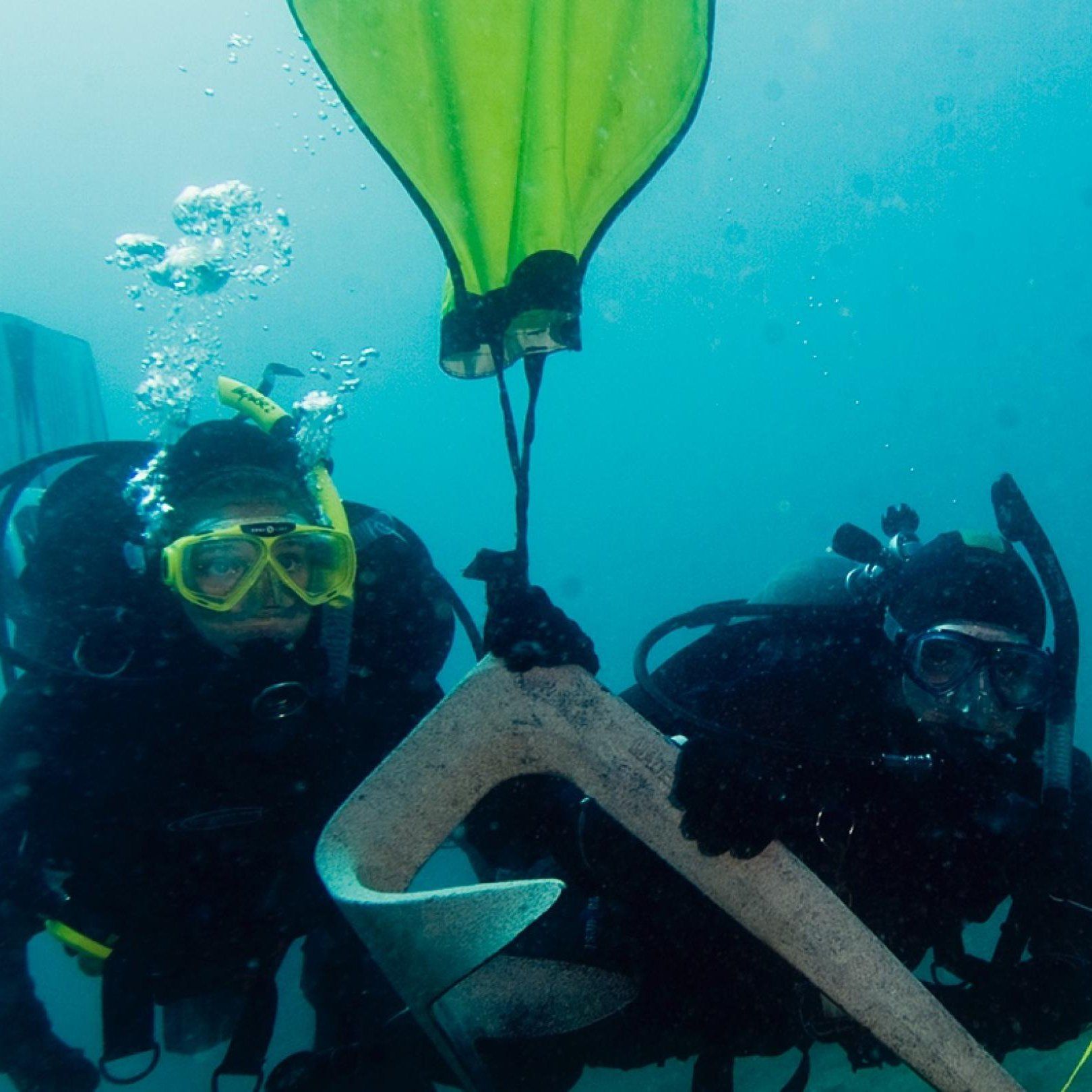 Two scuba divers underwater lifting a large, curved object, with a yellow lift bag above.