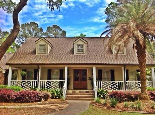 CertainTeed Shingle — House with CertainTeed Roofing in Savannah, GA Beige house with a wraparound porch, brown roof, and dormers. Palm tree and landscaping in front.