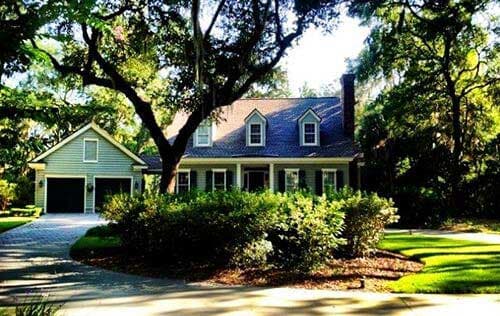 Luxury Shingles — Beautiful House in Savannah, GA House with gray siding and roof, green lawn, driveway, and large trees.