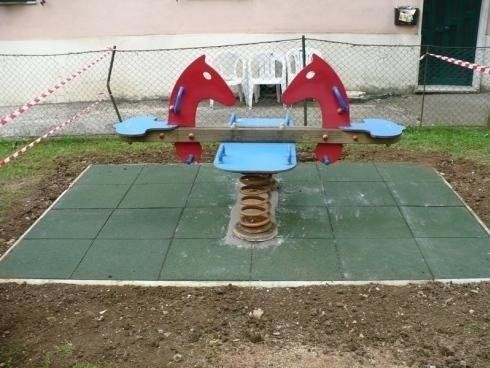 Un'altalena a molle rossa e blu per bambini è posizionata su una superficie rivestita di gomma verde in un'area giochi all'aperto.