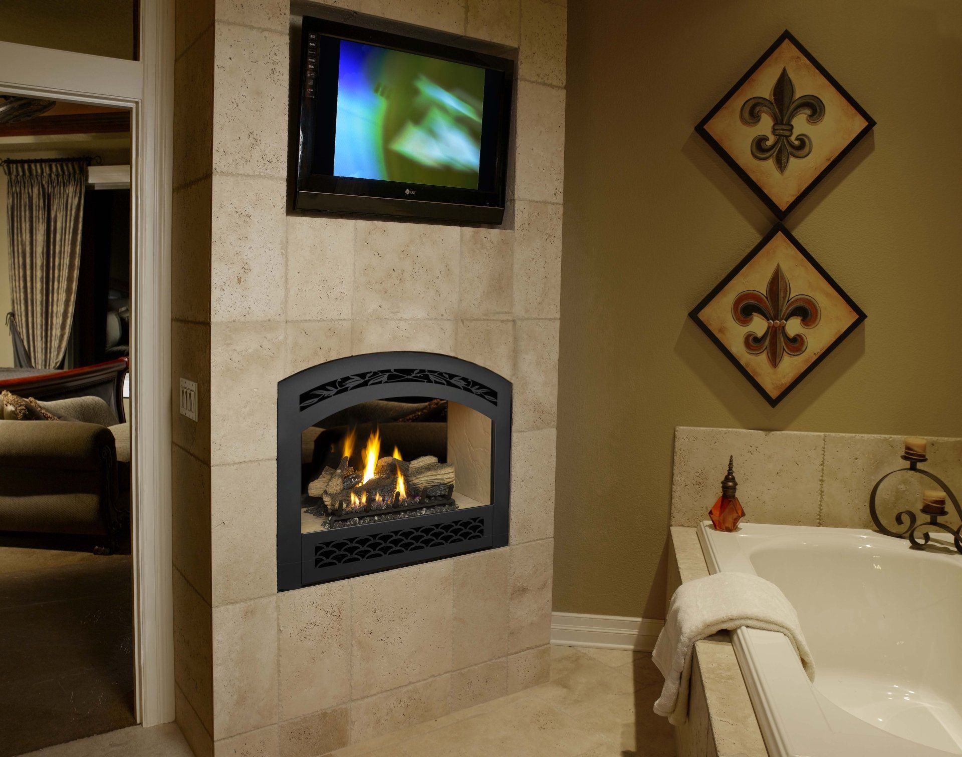 Bathroom with fireplace, TV, and bathtub. Beige stone walls, green walls with fleur-de-lis art.