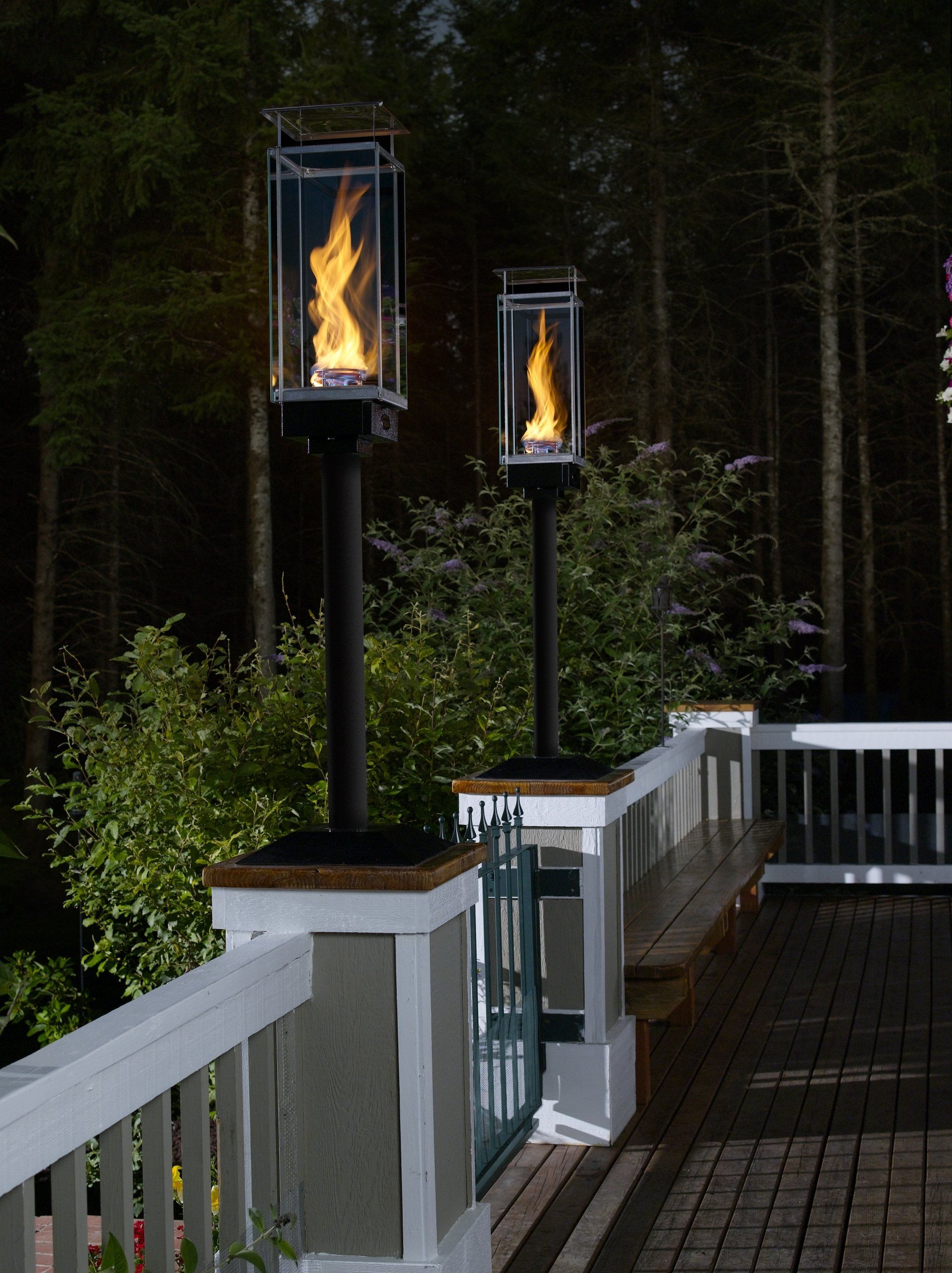 Two outdoor torches with flames on a deck, with trees in the background at night.