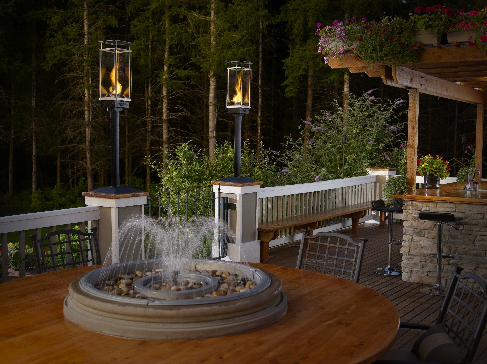 Outdoor deck at night with fire features, fountain, seating, and bar.
