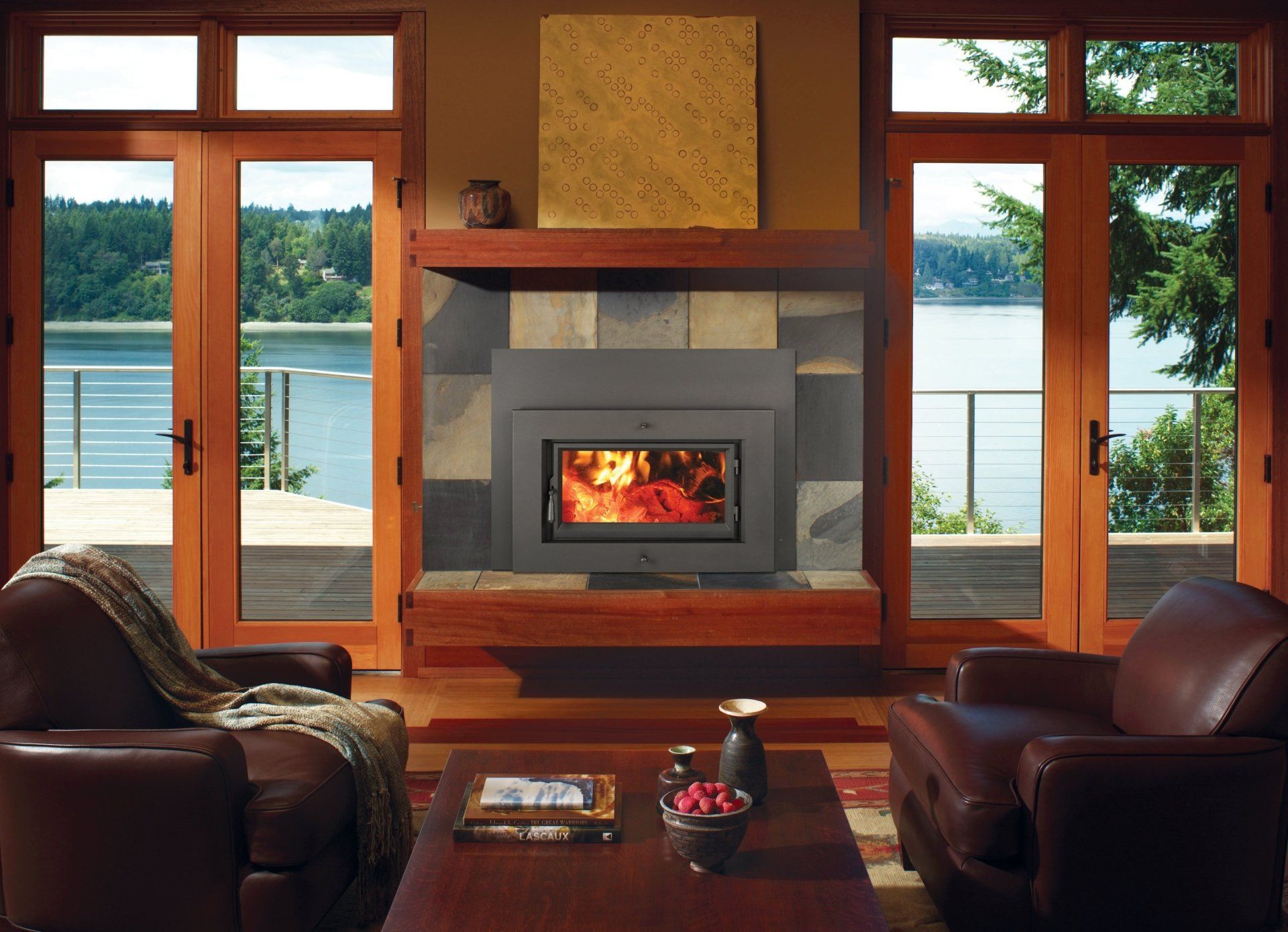 Cozy living room with fireplace, water view, leather chairs, wood trim, and open French doors.