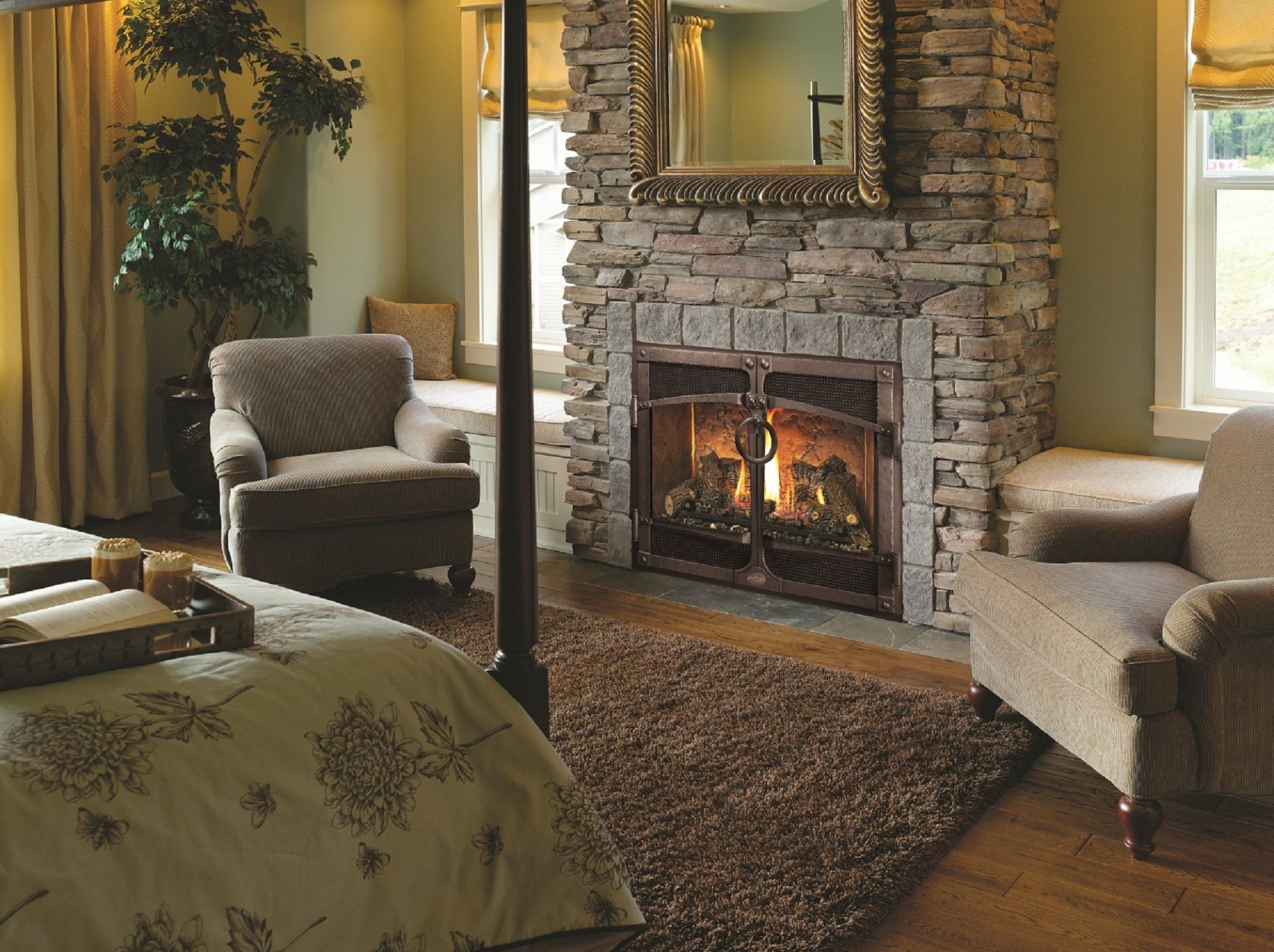 Cozy bedroom with stone fireplace, two armchairs, and a bed. Soft lighting, green walls, and a large window.