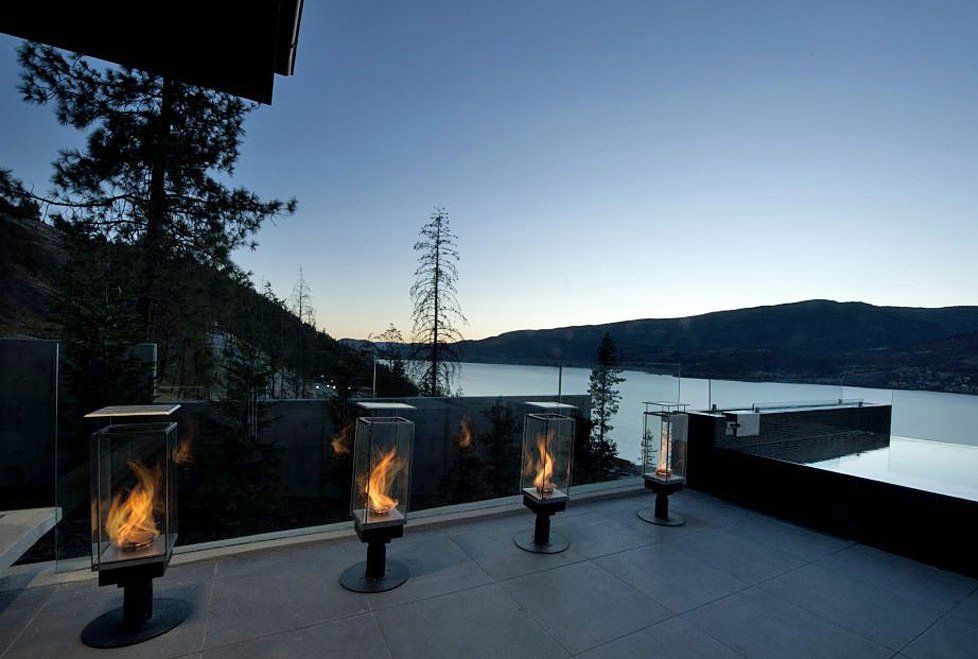 Outdoor patio at dusk with four lit fire lanterns overlooking a lake and hills.