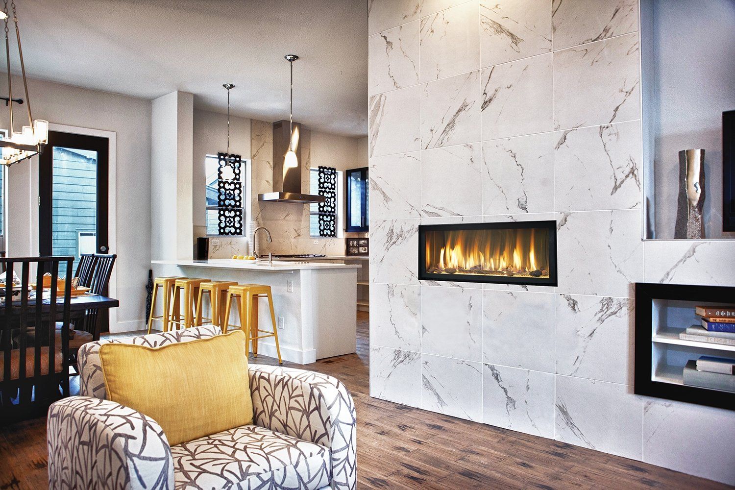 Modern living room with marble fireplace, open kitchen, and patterned armchair.