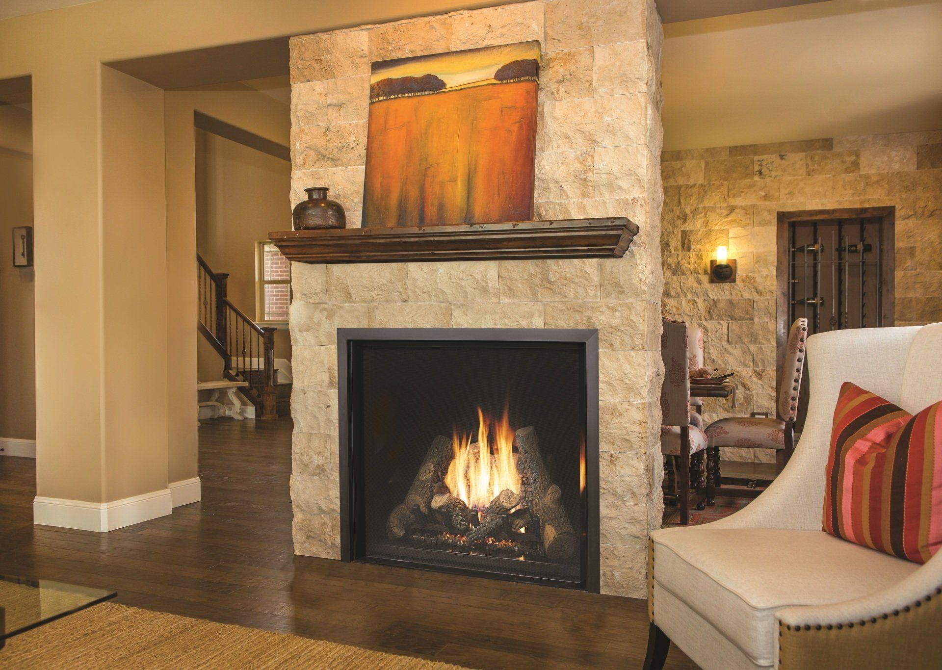 Fireplace with stone surround, lit flames, wooden mantel, and art in a living room.