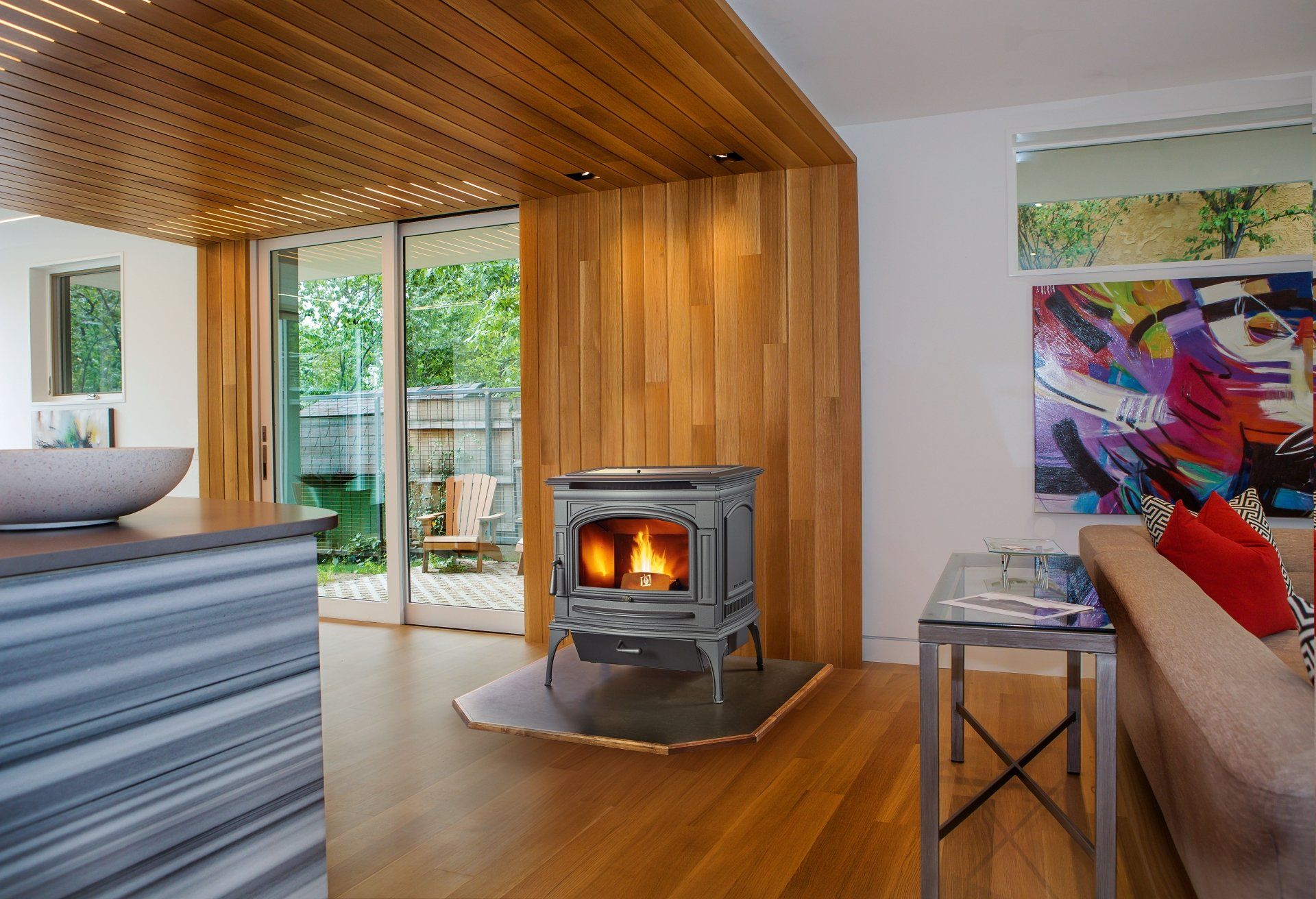 Cozy living room with a wood-burning stove, wooden walls and ceiling, and a view of a patio.