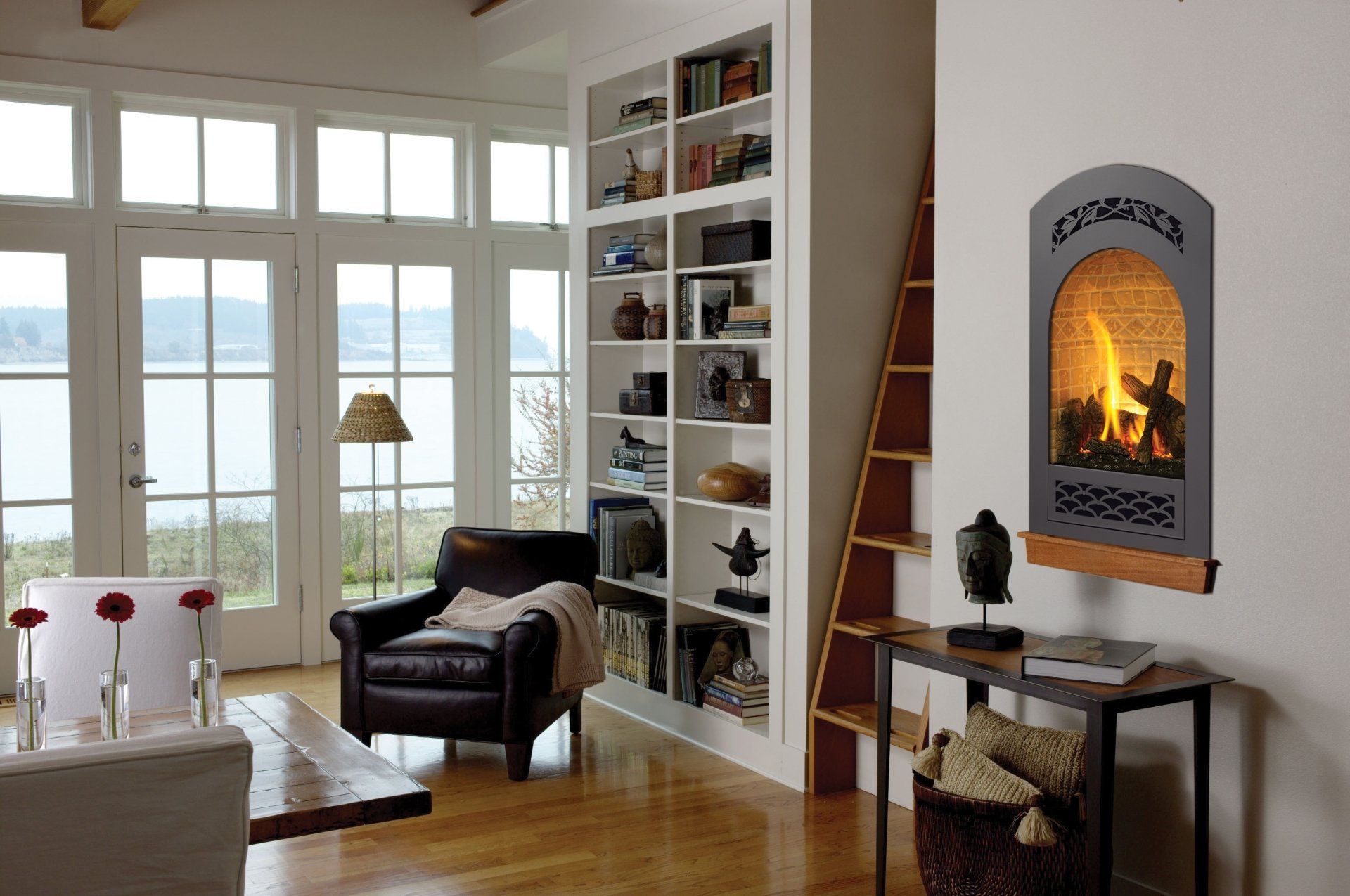 Living room with a fireplace, bookshelves, an armchair, and a view of water and trees.