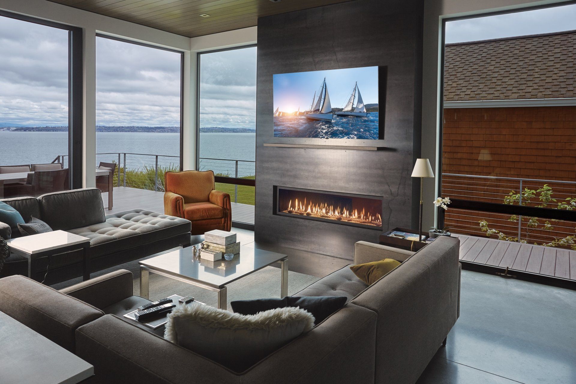 Modern living room with fireplace and water view. Large windows, sectional sofa, and a television.