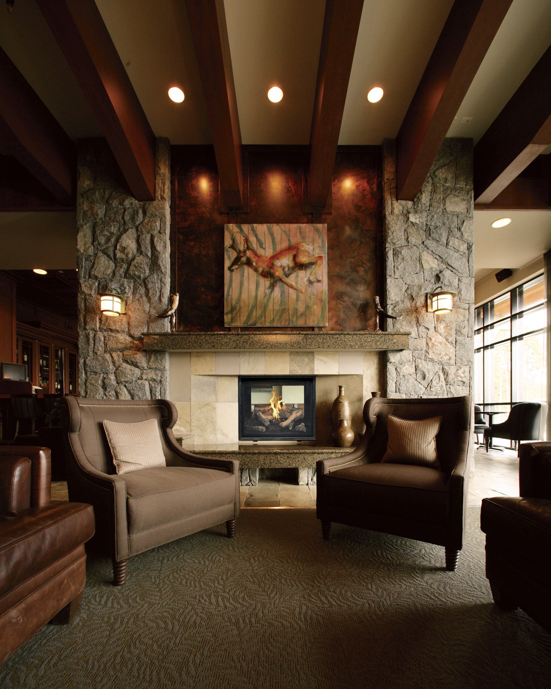 Stone fireplace with two brown armchairs in a cozy, well-lit living room.