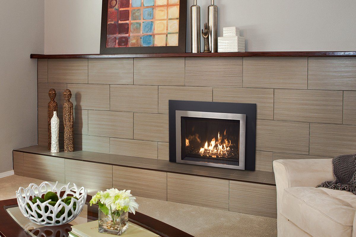 Fireplace with flames set in a stone wall with a wooden mantle; decorative items and a sofa nearby.