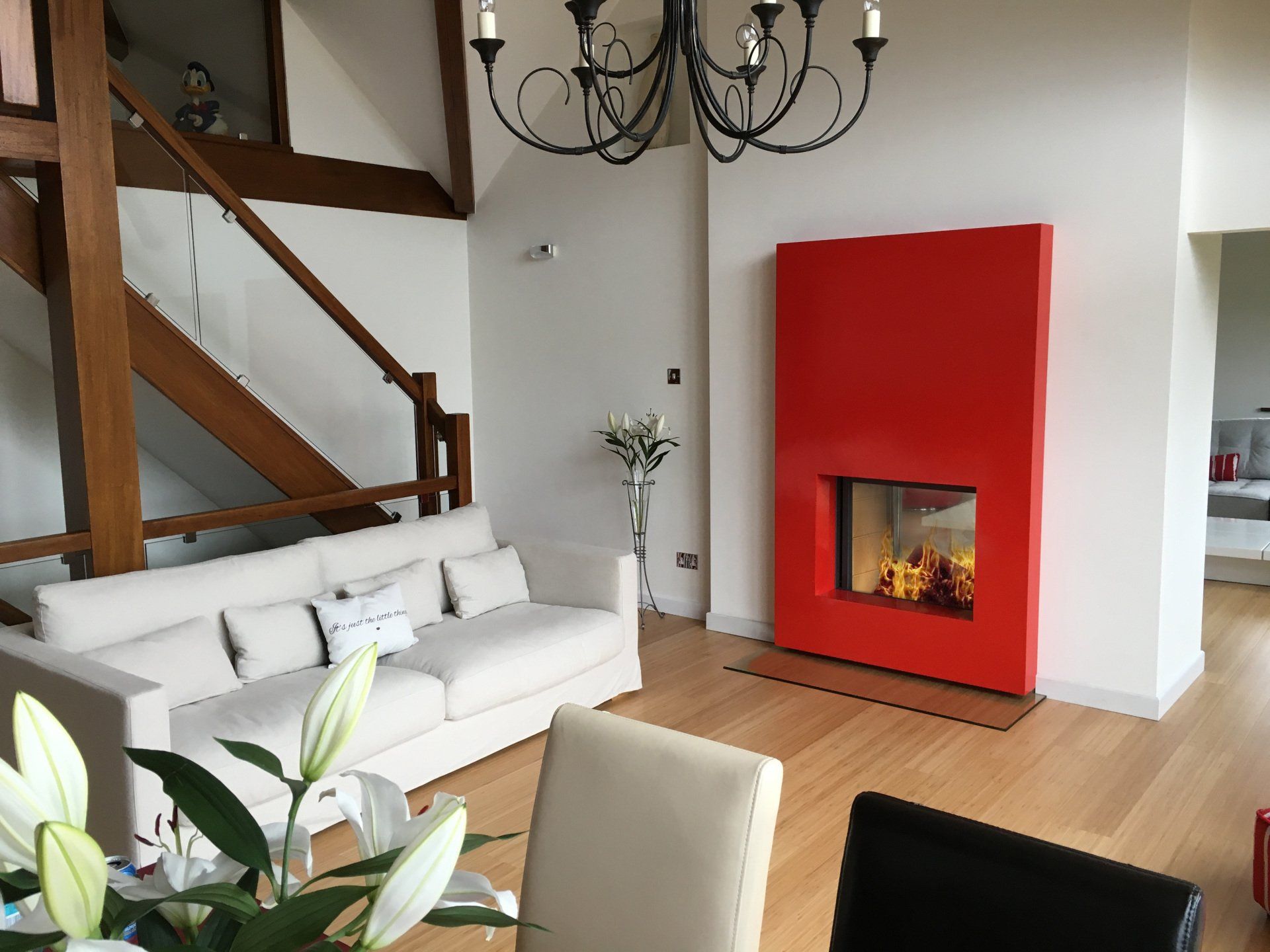 Living room with a modern red fireplace, white sofa, wooden beams, and a chandelier.