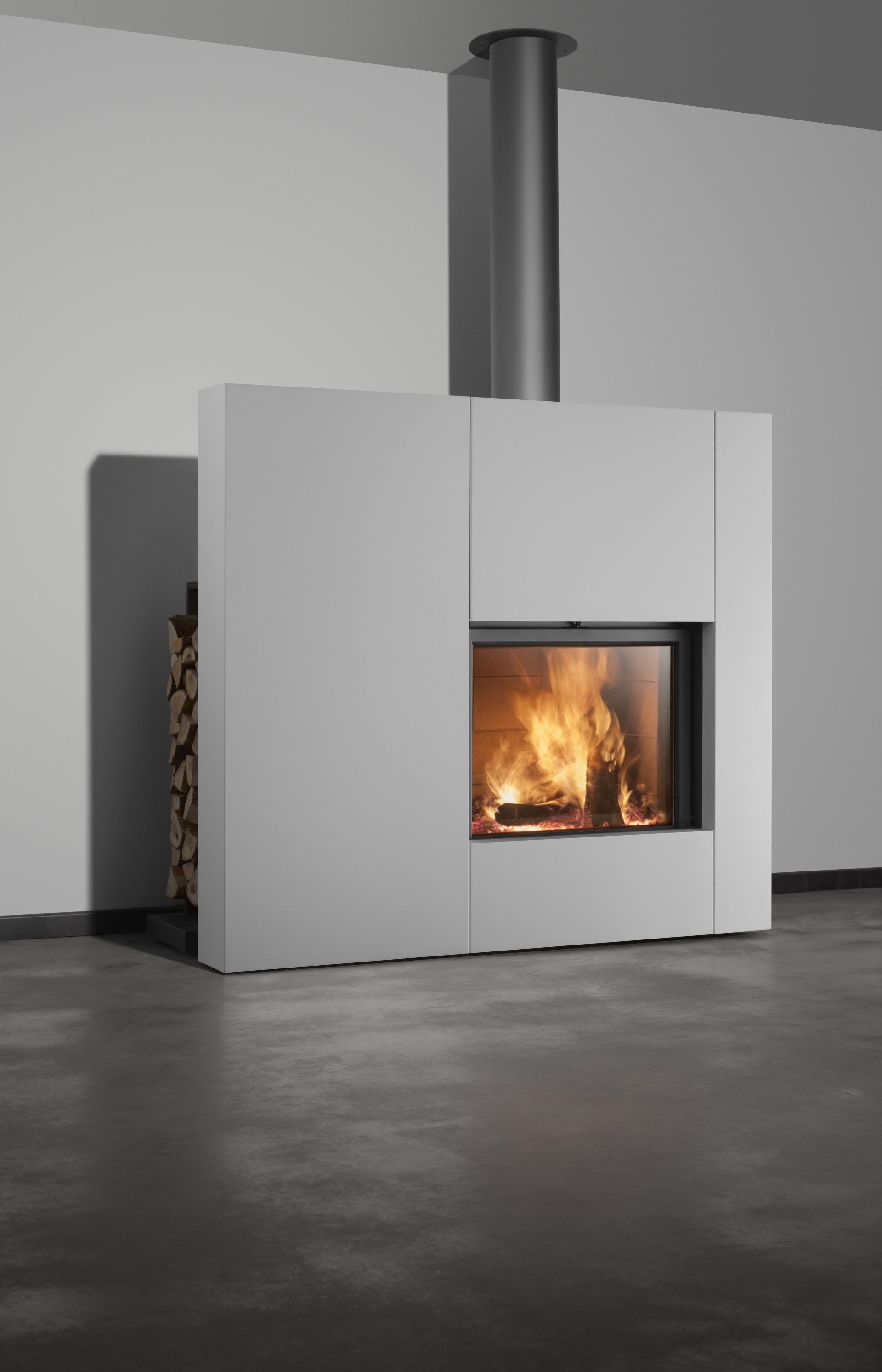 Modern fireplace with burning flames, gray surround, and metal chimney. Firewood stack on the side.