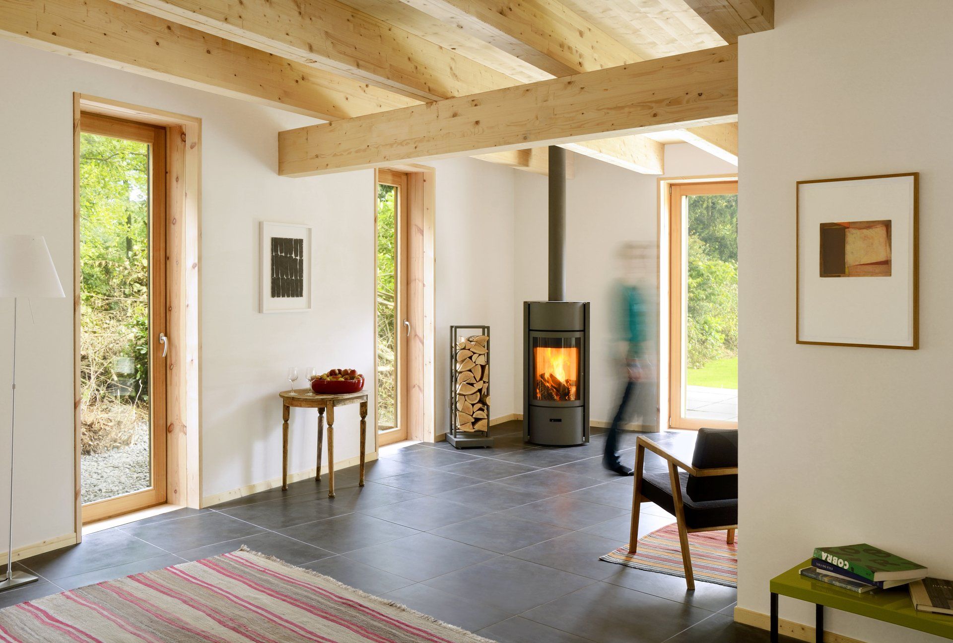 Bright living room with wooden beams, fireplace, and person walking.