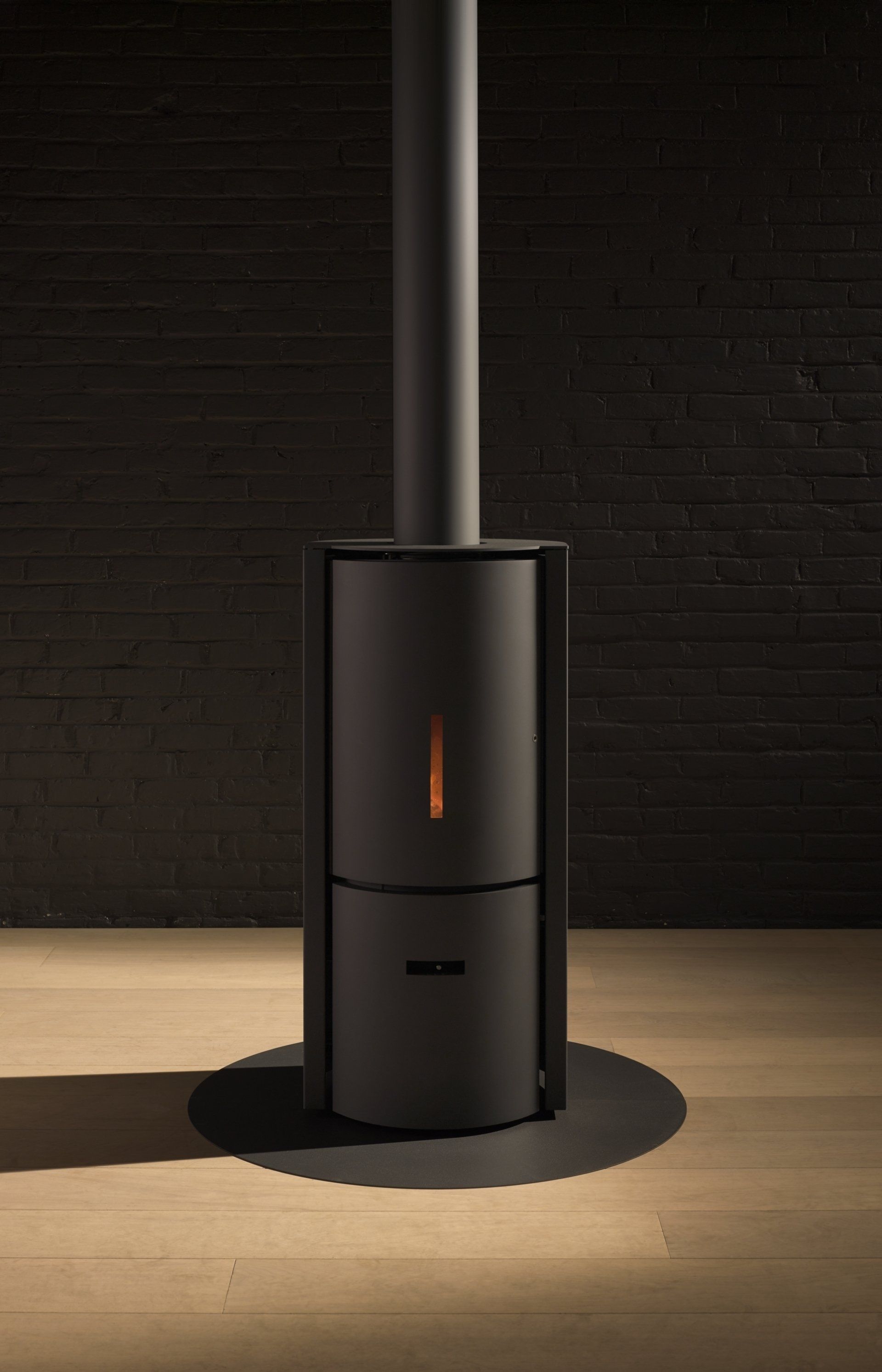 Black modern stove with chimney pipe against a black brick wall. The stove has a soft orange glow.