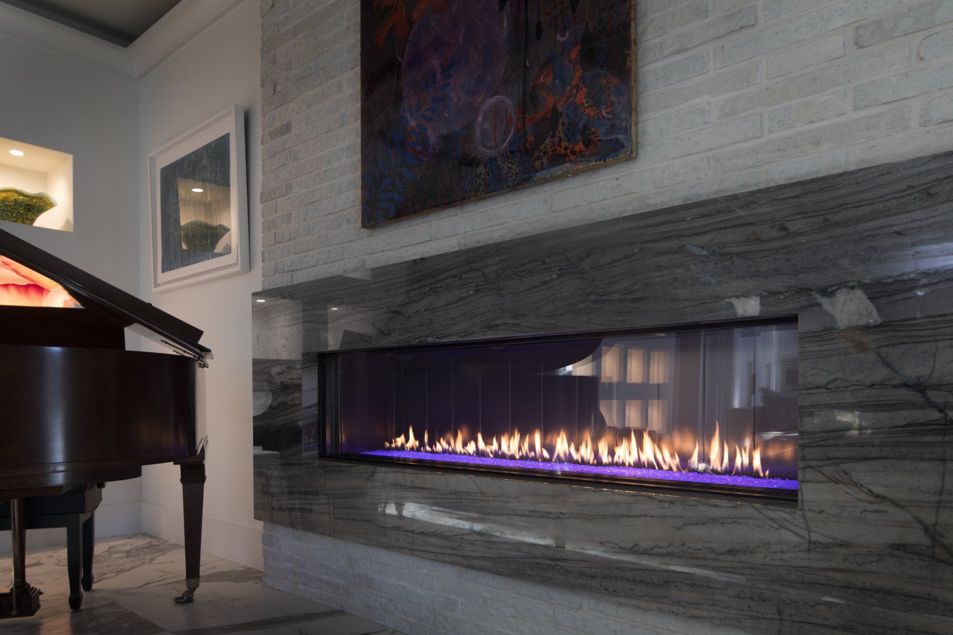 Modern living room with fireplace and grand piano. Fire burns inside a long glass structure.