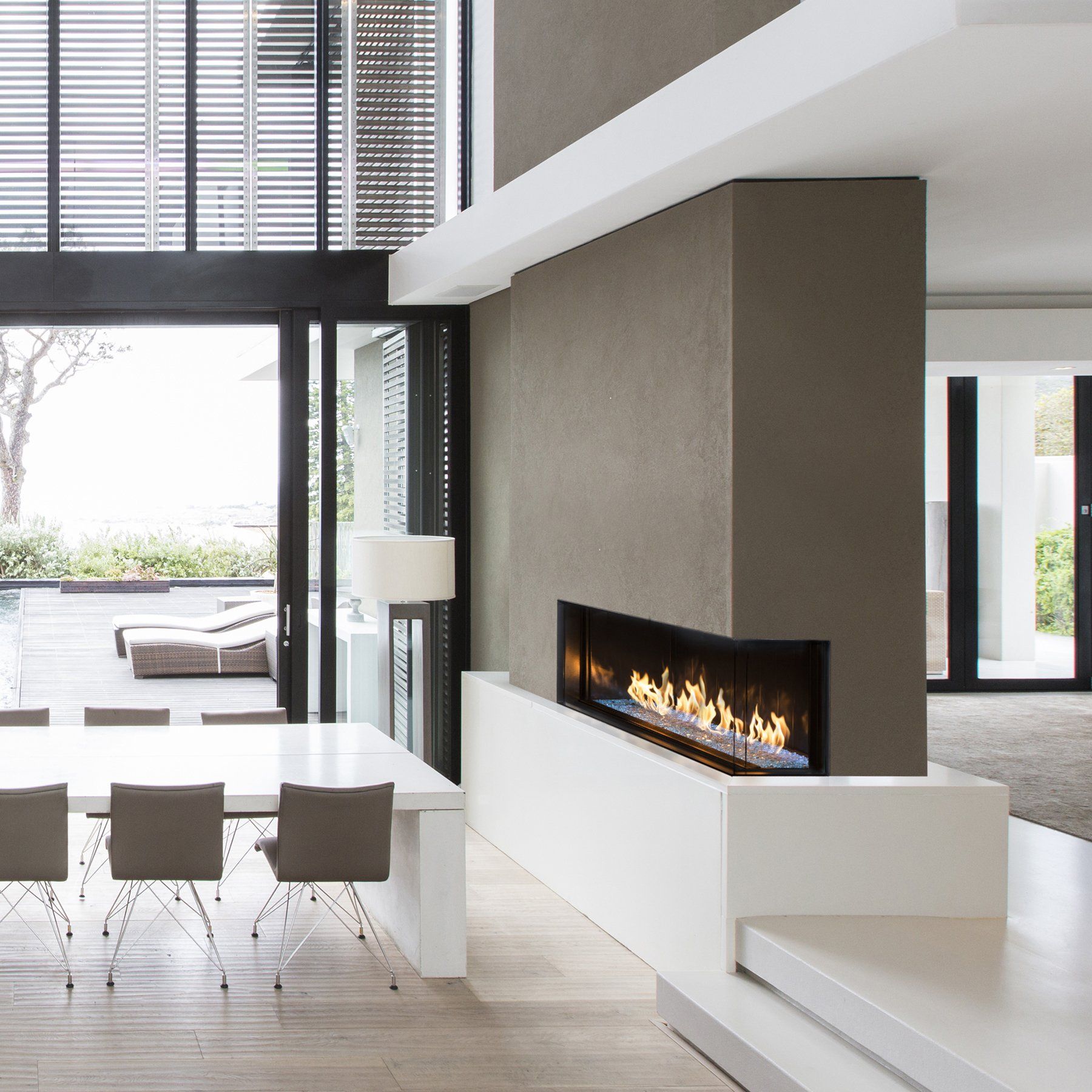 Modern living room with fireplace, dining table, and large windows overlooking a patio.