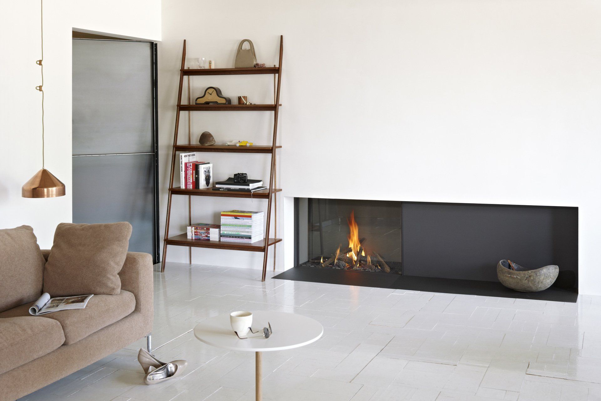 Modern living room with fireplace, shelving, and tan sofa, against white walls and flooring.