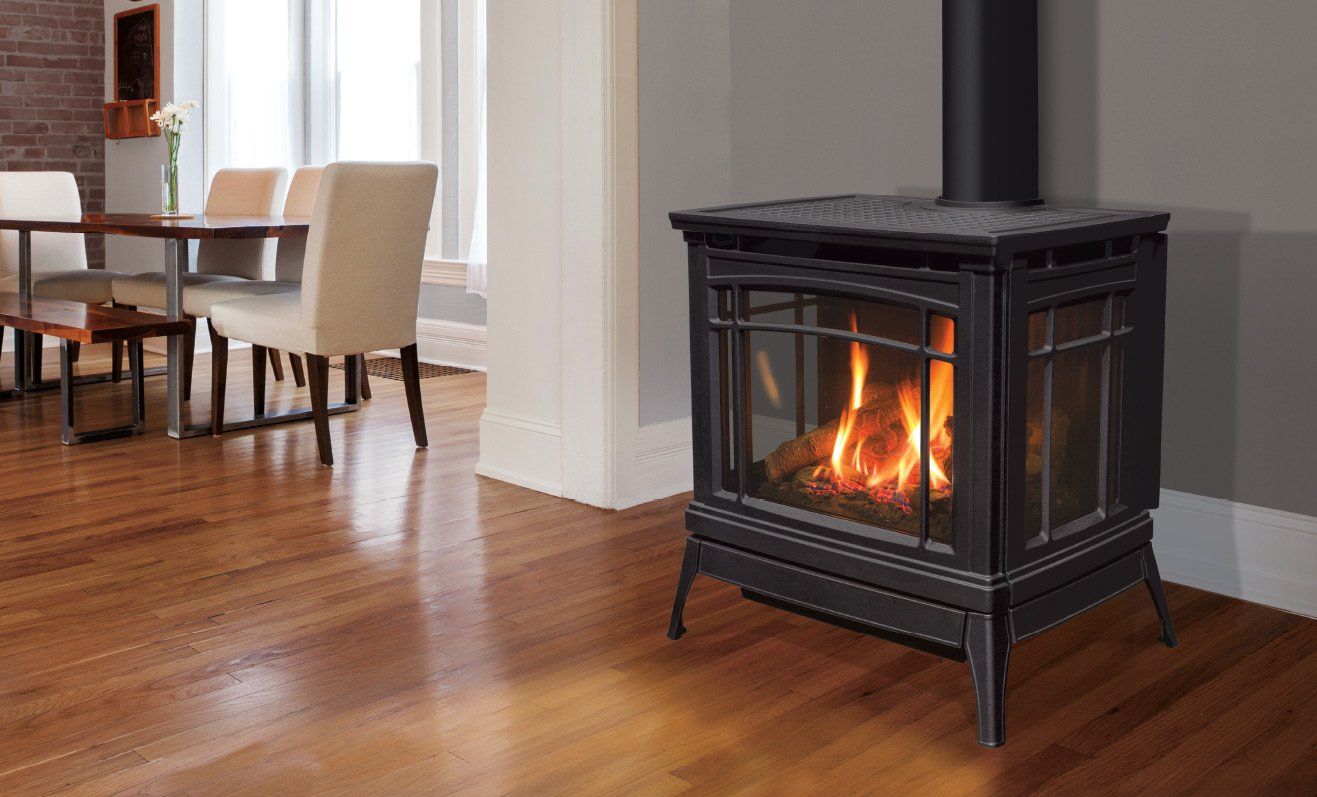 A lit gas fireplace in a room with hardwood floors, near a dining table.