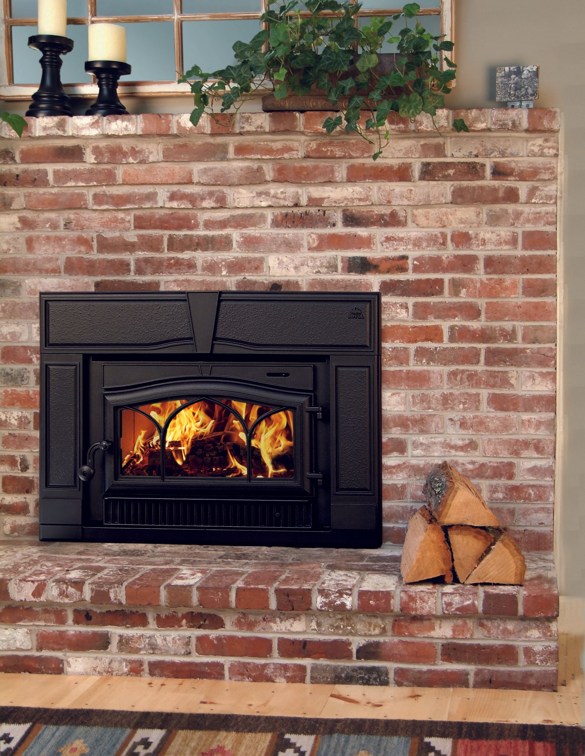 A brick fireplace with a lit fire, wood stack, and decor.