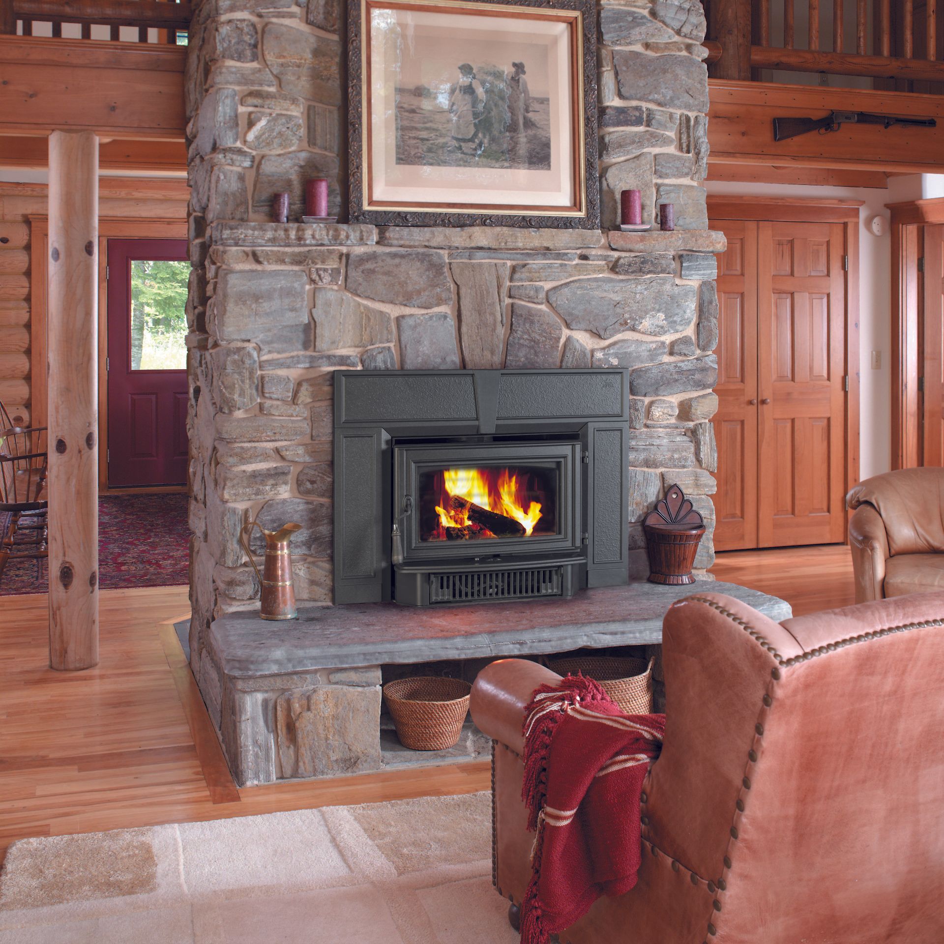 Stone fireplace with a burning fire, a painting above, and a leather armchair.