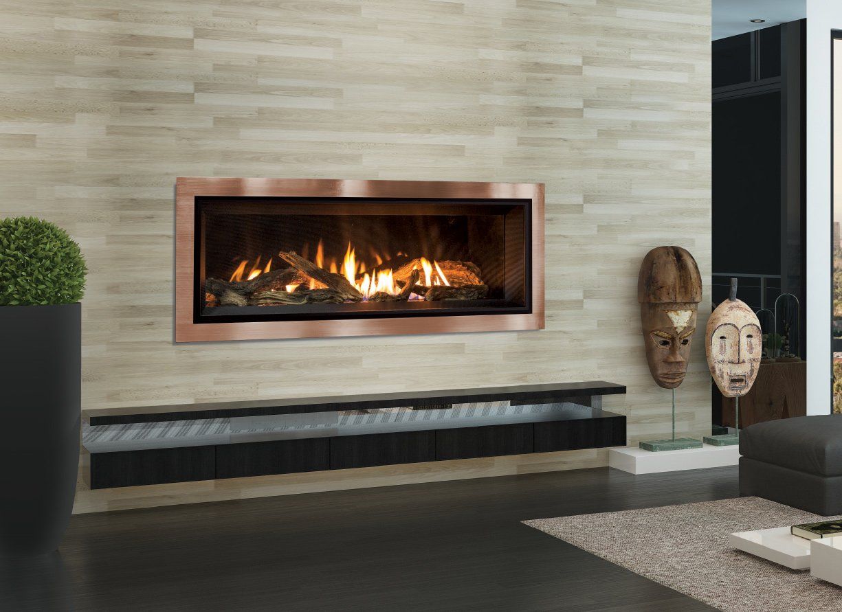 Copper-framed fireplace on a neutral stone wall, with a floating black shelf and decorative masks nearby.