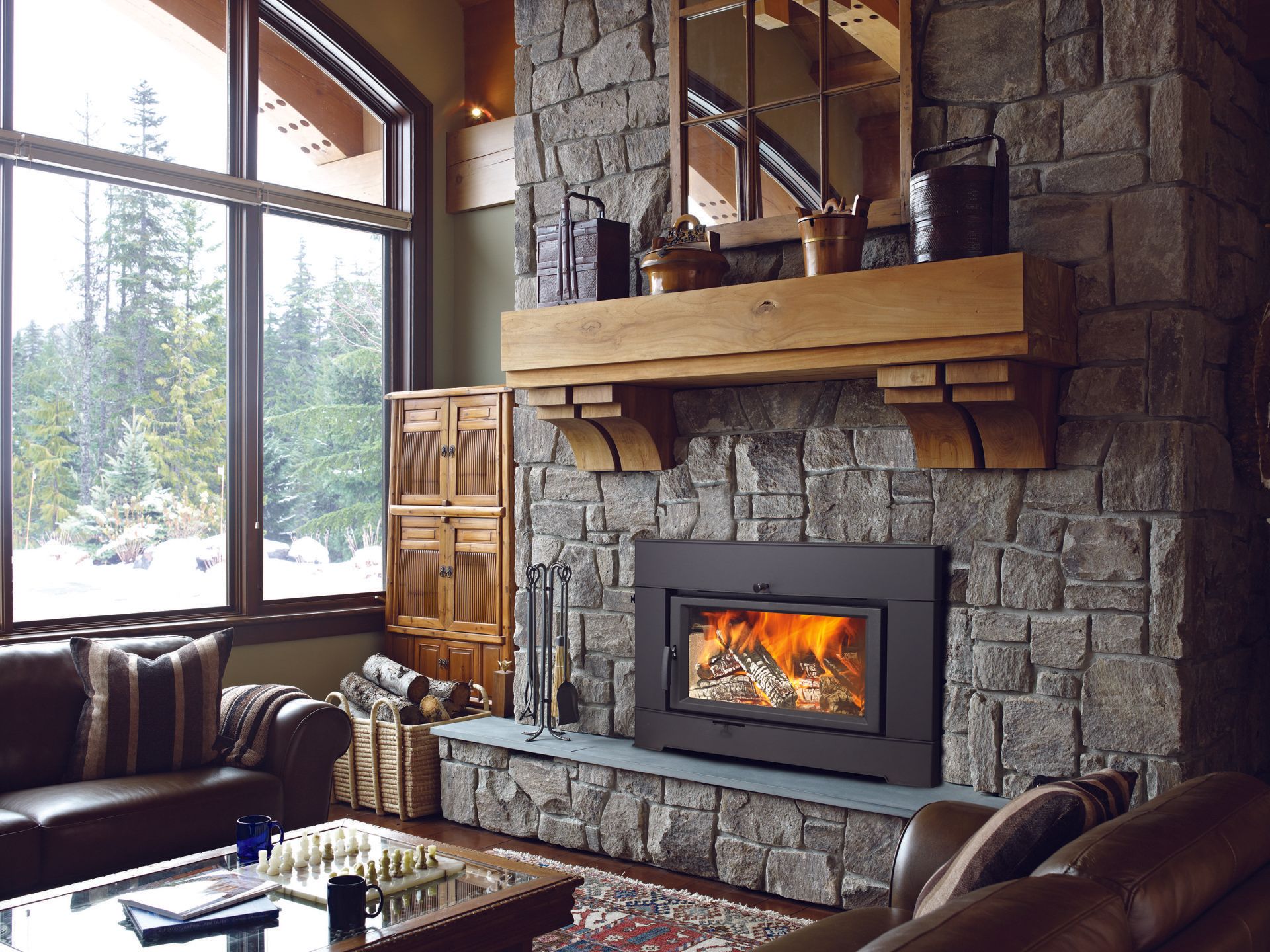 Living room with stone fireplace, wood mantle, fire burning, and large window.
